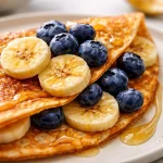 Small-Batch Protein Banana Crepes served with fresh fruit and syrup.