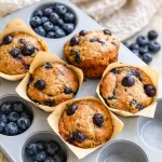 Healthy Blueberry Cottage Cheese Muffins in a muffin tin with fresh blueberries.